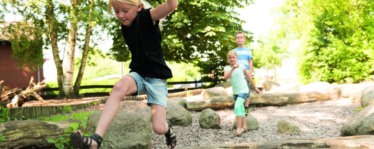Grundschulkinder spielen auf einem naturnahen Außengelände