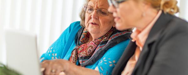 Frau erklärt einer Seniorin etwas am PC