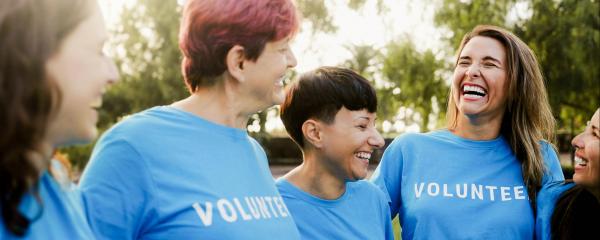 Menschengruppe mit t shirt mit der Aufschrift Volunteers stehen eingehakt nebeinander und lachen 
