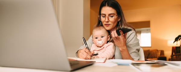 Arbeitende Frau am Schreibtisch mit Kind auf dem Schoß